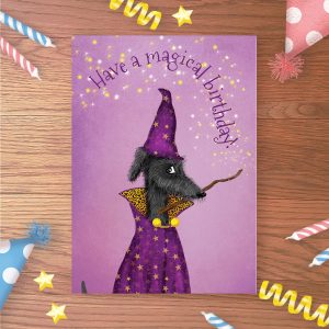 Birthday card with a shaggy black dog wearing purple wizard's robes and holding a magic wand in his mouth, with 'Have a magical birthday!' flowing from the wand.