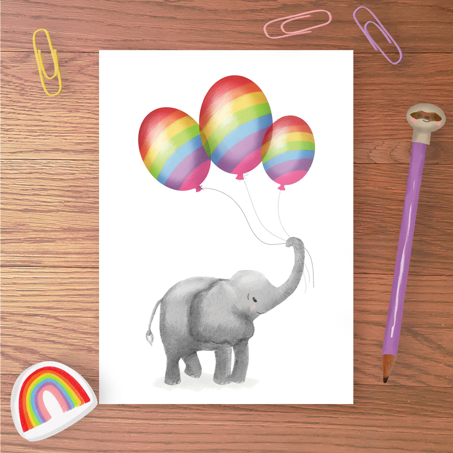 Greetings card with a baby elephant holding three rainbow balloons in his trunk.