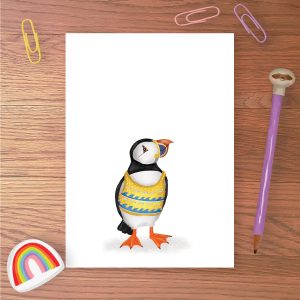 Greetings card with a puffin wearing a yellow and blue knitted tanktop with a wave pattern on it.