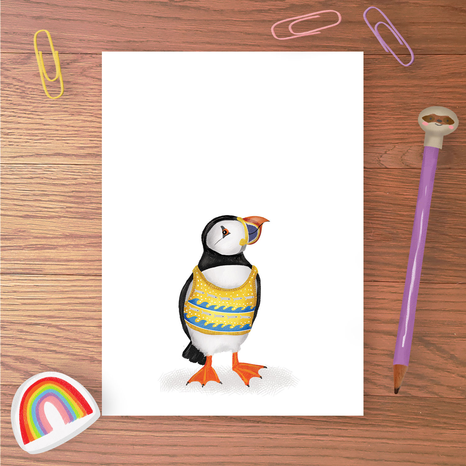 Greetings card with a puffin wearing a yellow and blue knitted tanktop with a wave pattern on it.