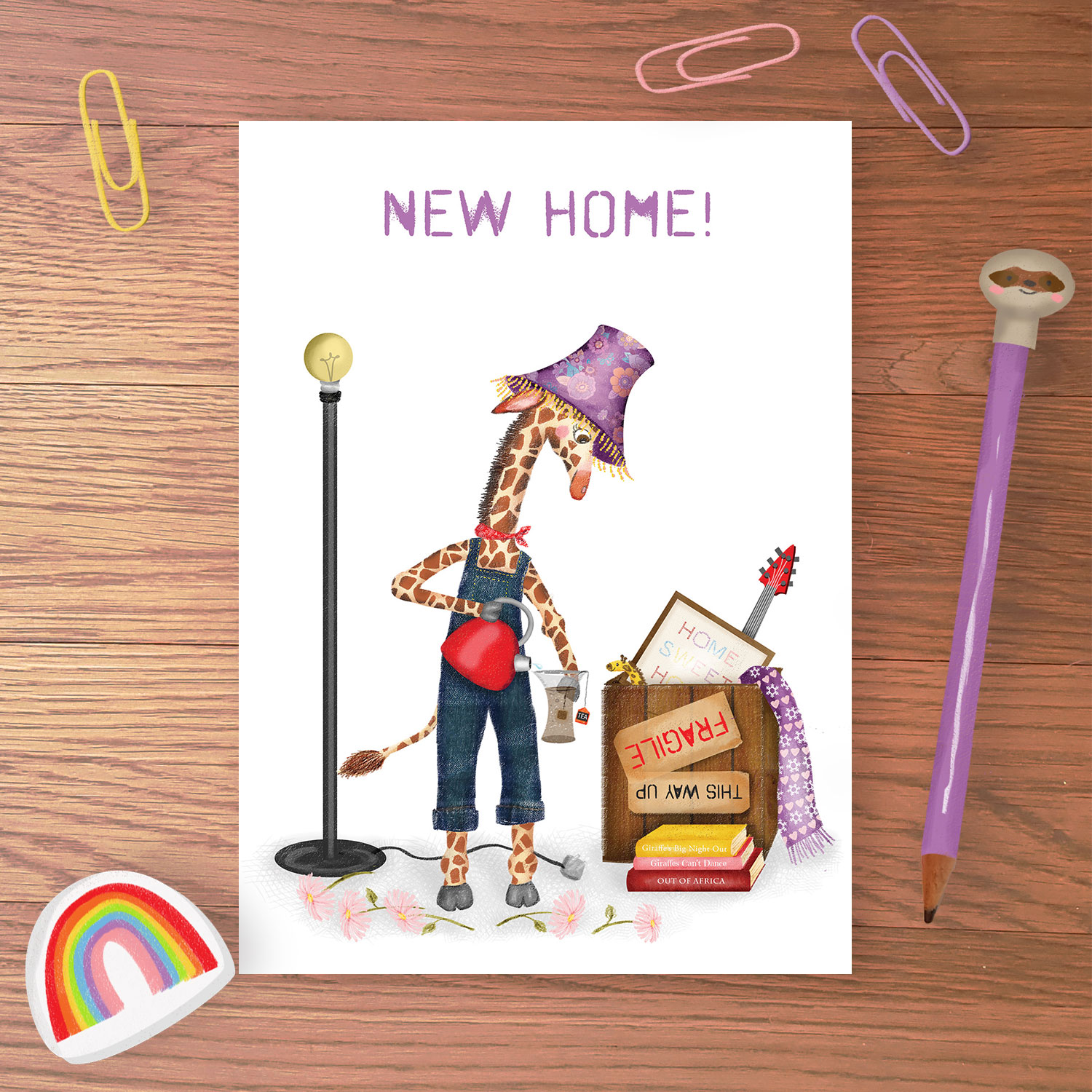 Greetings card with a giraffe with a lampshade on his head, making tea in a vase, with a packing case behind him and NEW HOME written above,