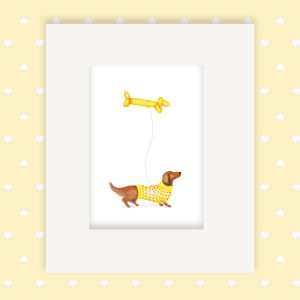 Mounted print hanging on a wall, of a dachshund wearing a yellow jumper, holding a sausage dog balloon.
