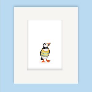 Mounted print hanging on a wall, of a puffin wearing a yellow and blue knitted tanktop.