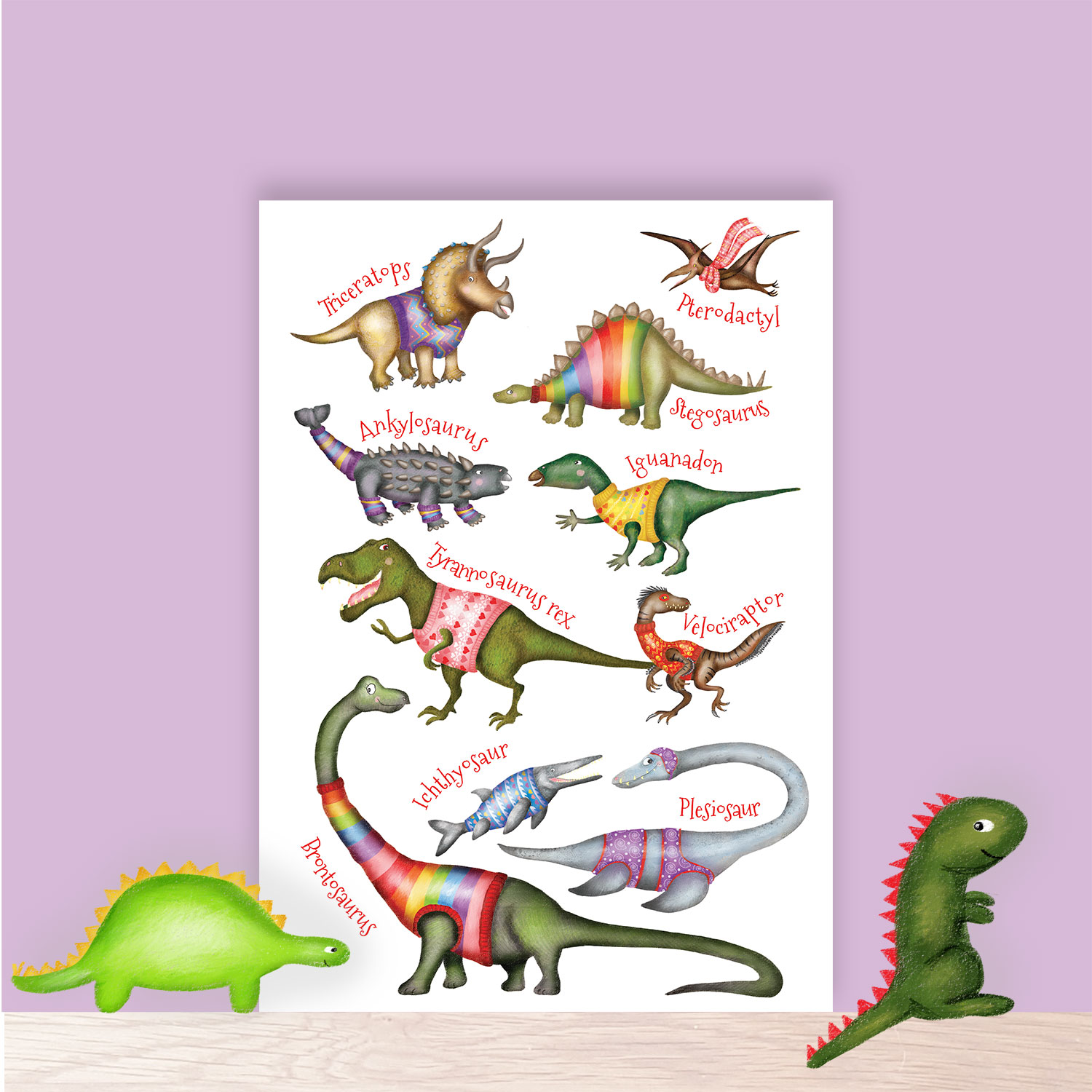 Fun colourful A4 print of dinosaurs wearing jumpers; sitting on a shelf with toys.