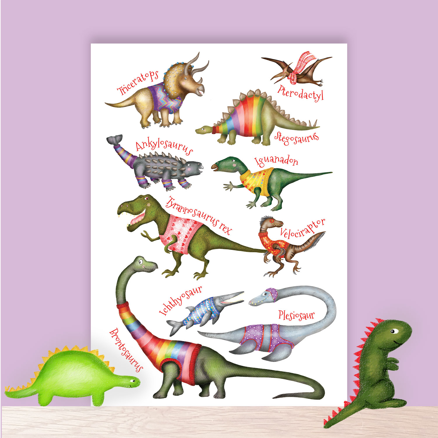 Print of cute dinosaurs wearing colourful jumpers, sitting on a shelf with toy dinosaurs next to it.