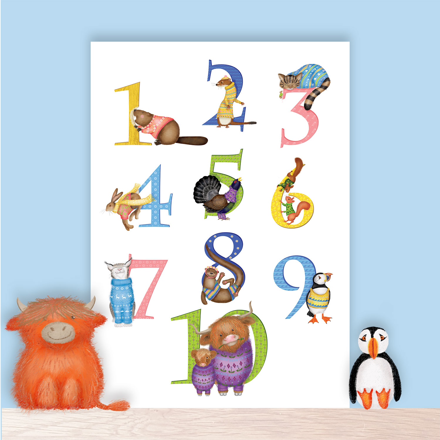 Print of the numbers 1-10 illustrated with Scottish animals, including Highland cows and a puffin. The print is sitting on a shelf with a highland cow and puffin toy,