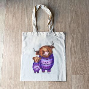 Tote bag with a drawing of a mother Highland coo and calf, both wearing purple jumpers patterned with thistles.